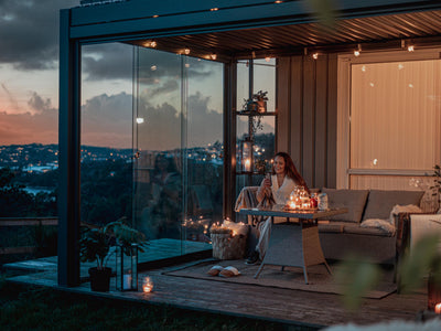 Woman sitting at a table under a modern pergola with cityscape view during dusk.