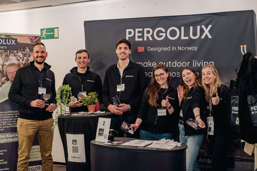 Group of PERGOLUX employees posing in front of a Pergolux banner at an event.