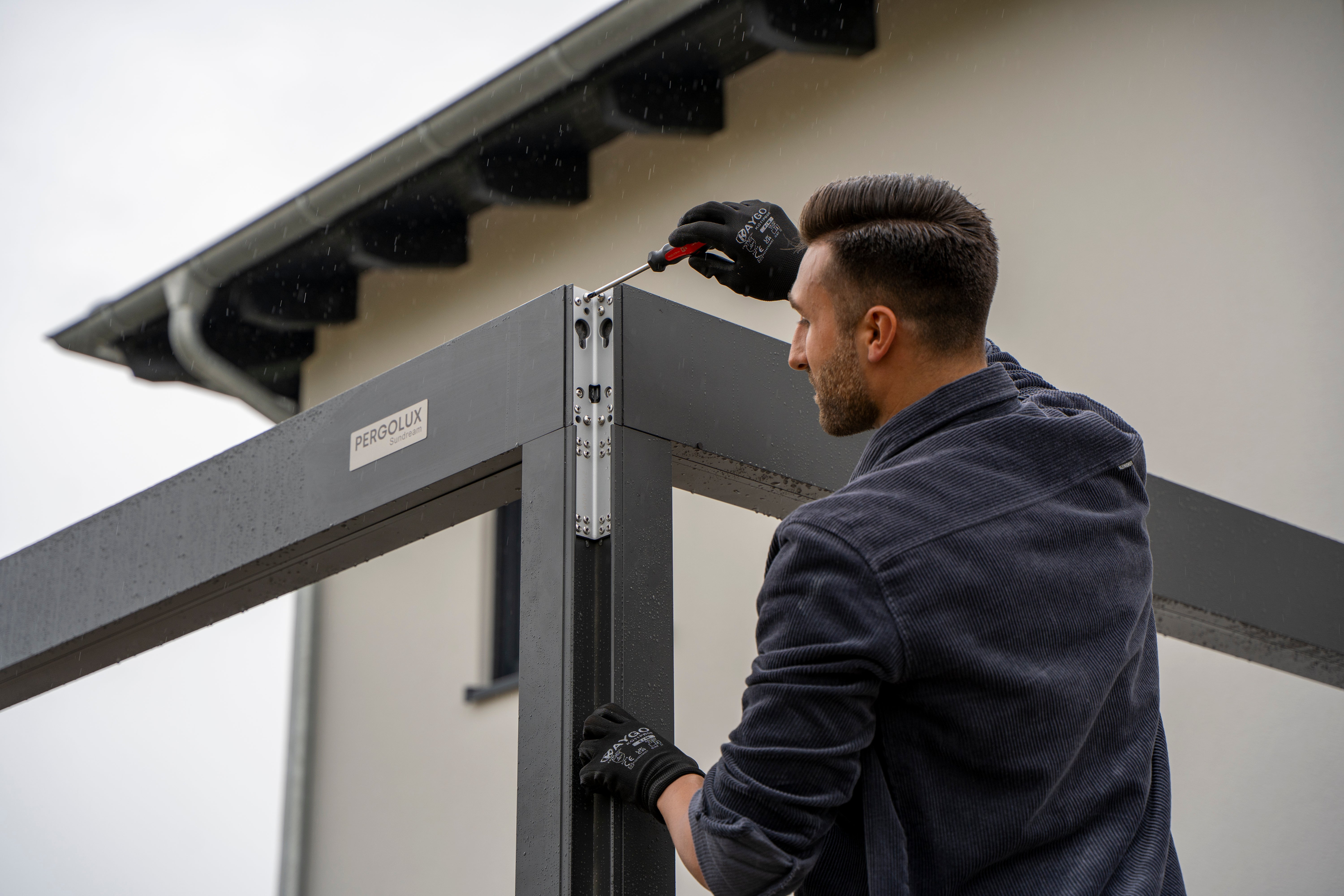 Person installing a metal pergola frame on a building exterior