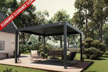 A dark gray outdoor patio cover with integrated roof shading and four support posts, set on a wooden deck in a landscaped backyard with lawn, trees, and patio furniture. A red diagonal banner reading 'CLEARANCE CLEARANCE' is overlaid across the top left.