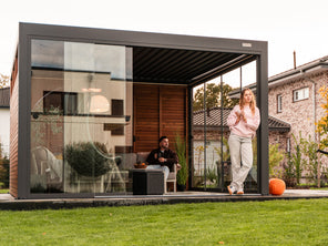 Modern outdoor office with glass walls and people inside, surrounded by greenery.