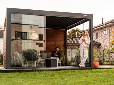 Modern outdoor office with glass walls and people inside, surrounded by greenery.