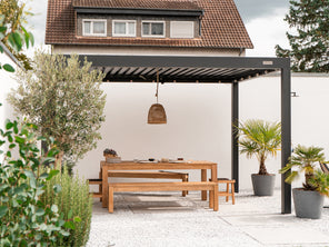 Outdoor patio with wooden dining set under a pergola, surrounded by plants.