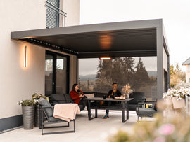 People sitting on a patio with a modern pergola and outdoor furniture.