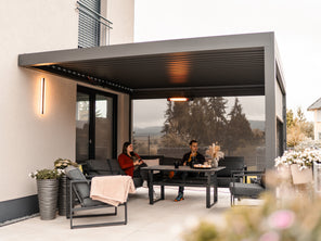 People sitting on a patio with a modern pergola and outdoor furniture.