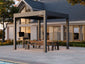 Paved patio with Pergolux Pro Max pergola, wood table, and chairs in front of a house at sunset