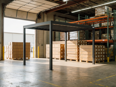 Warehouse interior with a metal PERGOLUX and stacked pallets of boxes.